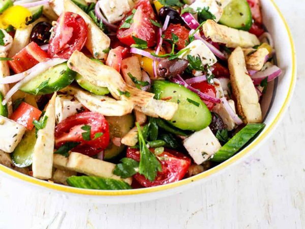 Bowl of Greek salad with tomato, cucumber, feta, red onion and toasted pita