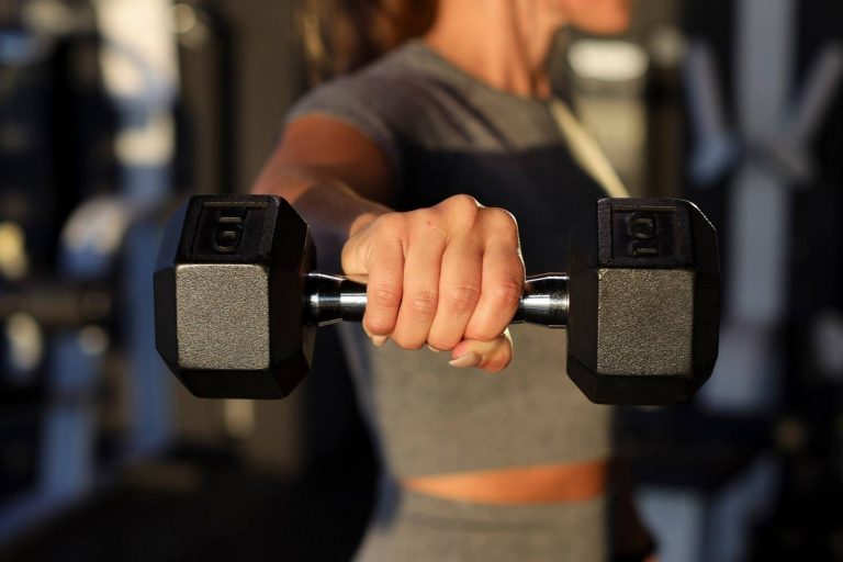 Close-up of a woman holding a 10 kg dumbbell out at arm's length in the gym