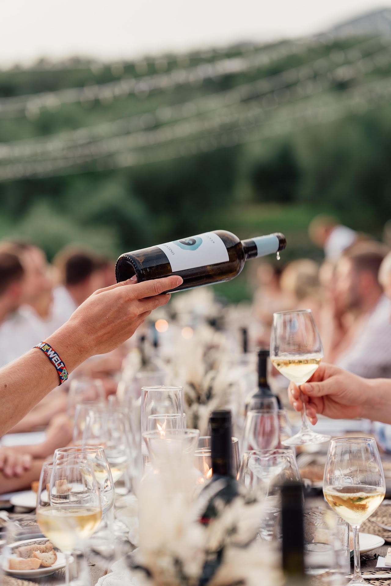 Bottle of white wine being poured at a long outdoor dinner table at dusk