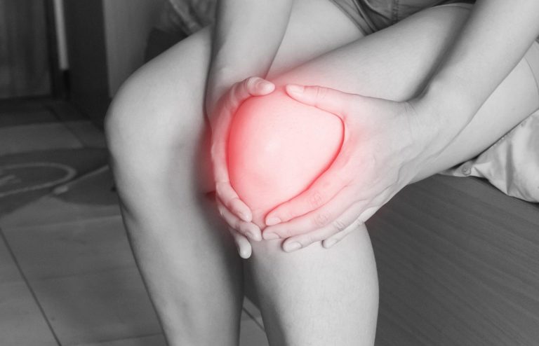 Person sitting and holding their knee, with the sore area highlighted in red