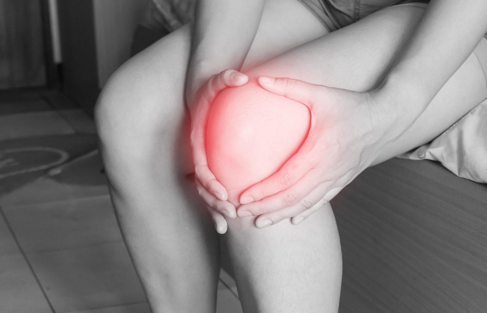 Person sitting and holding their knee, with the sore area highlighted in red
