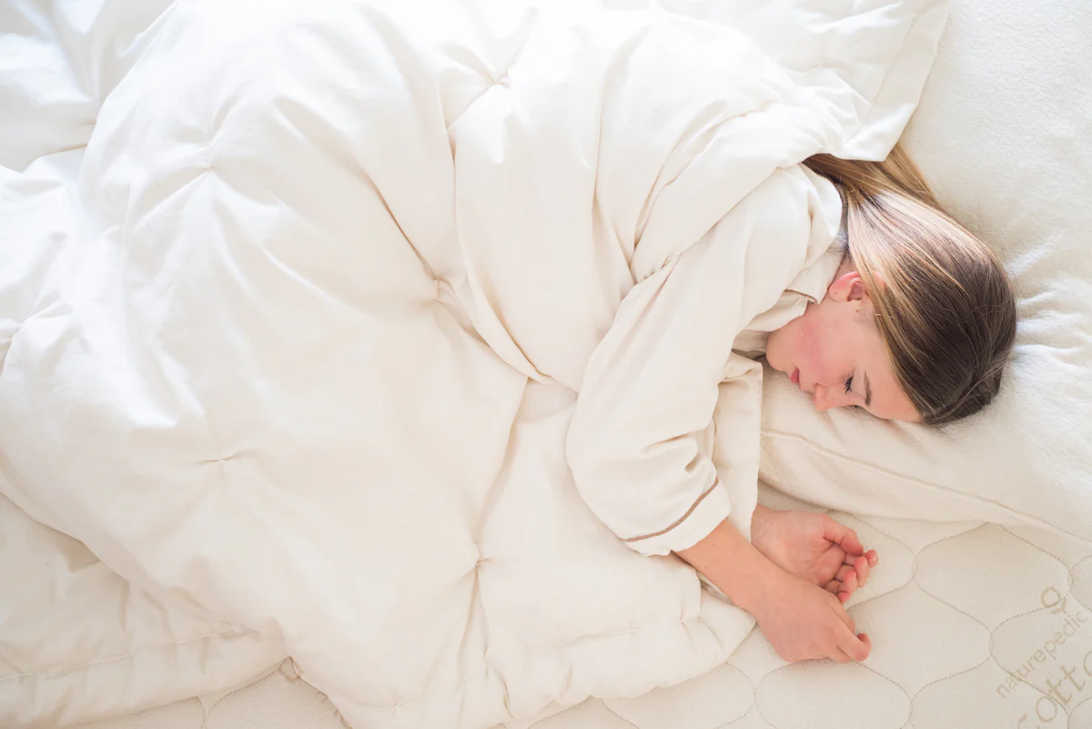 Woman asleep in bed under a white doona, seen from above