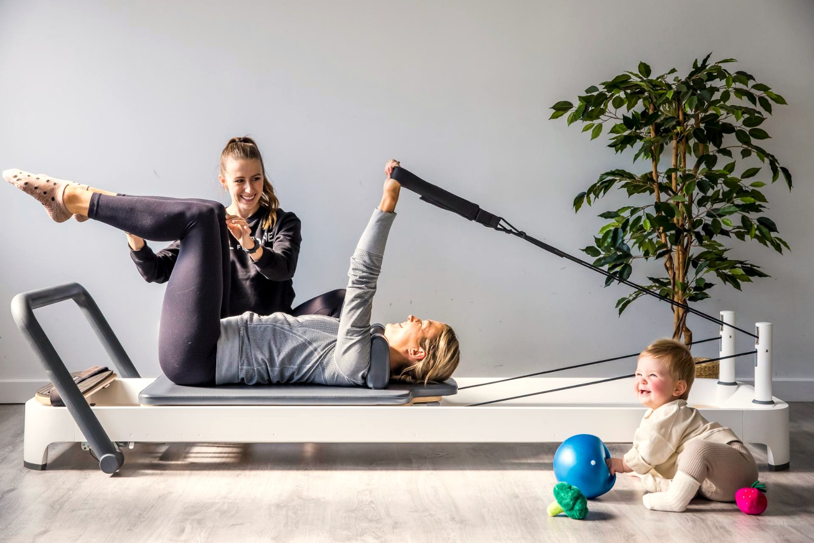 Parent exercising on a reformer with her baby beside her in a Mums and Bubs class