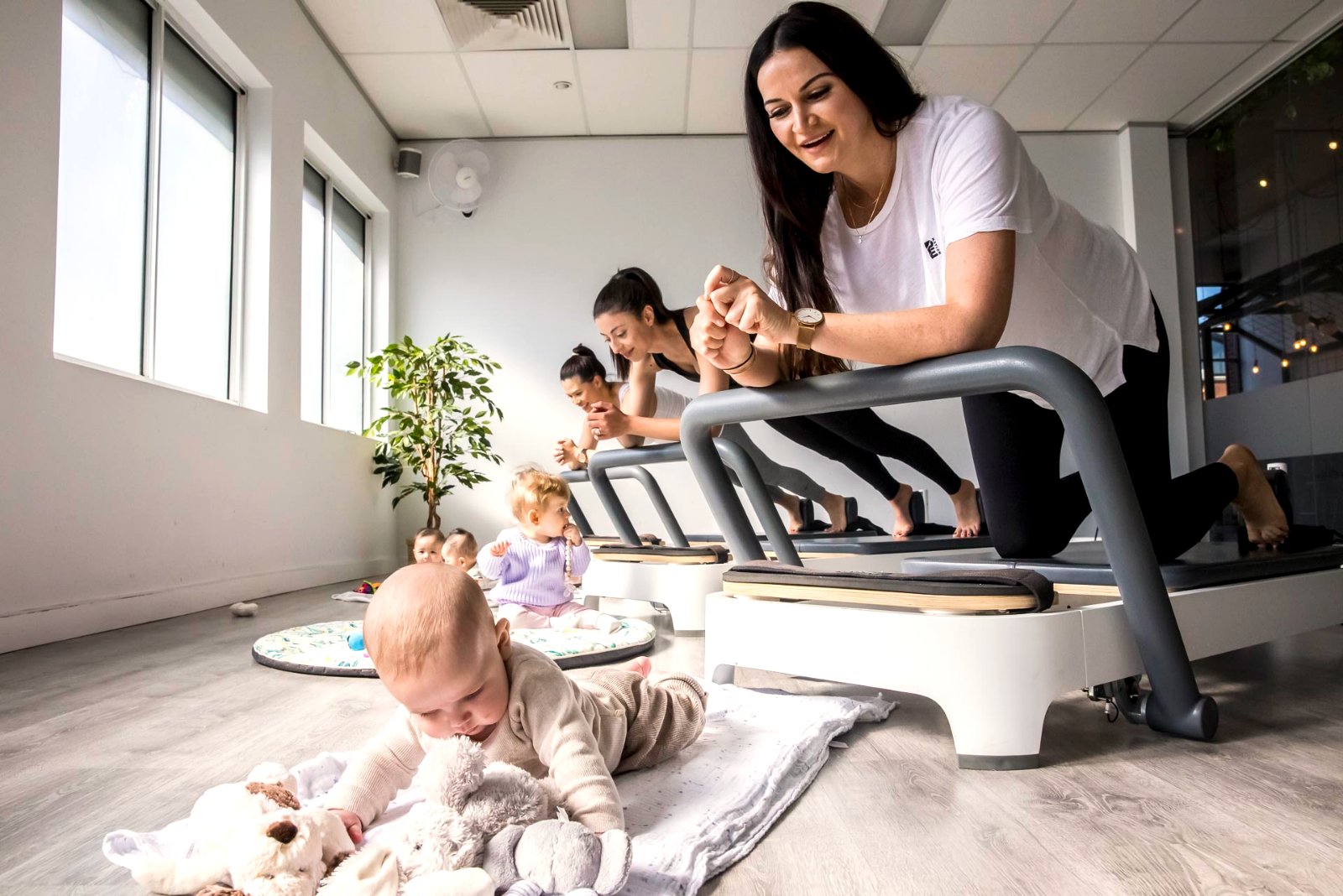 A new mum mid-exercise on the reformer with her baby beside her at All for One