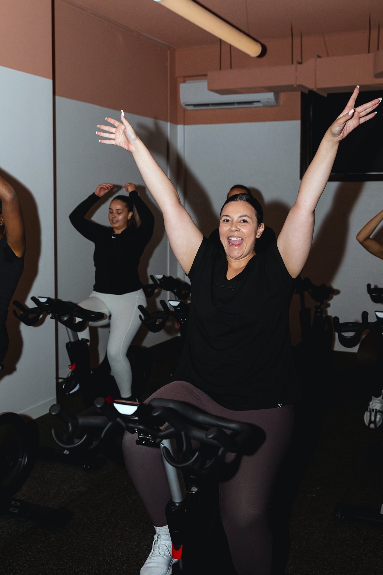 Rider with arms raised celebrating at the end of a spin class