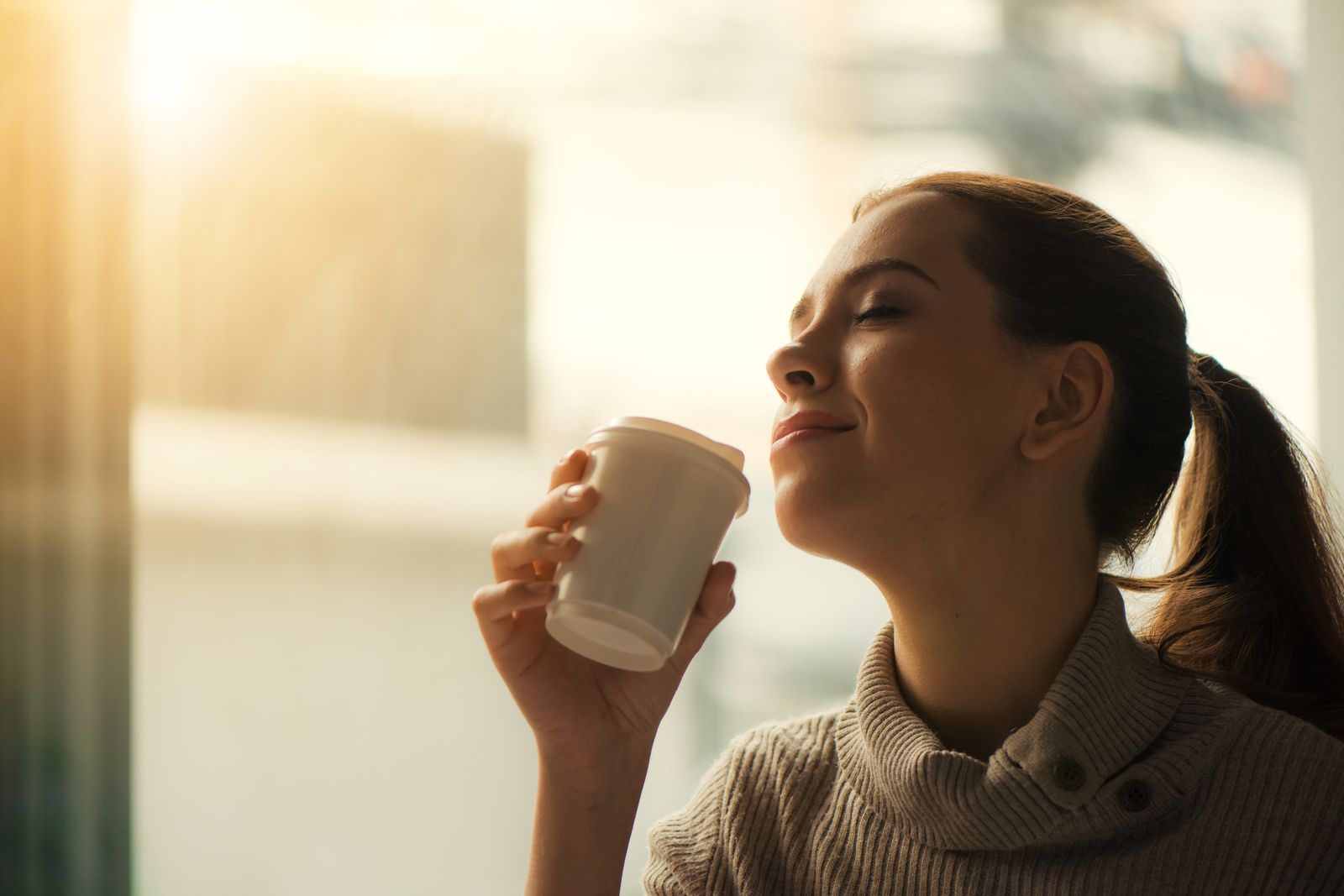 Woman holding a coffee in warm morning sunlight