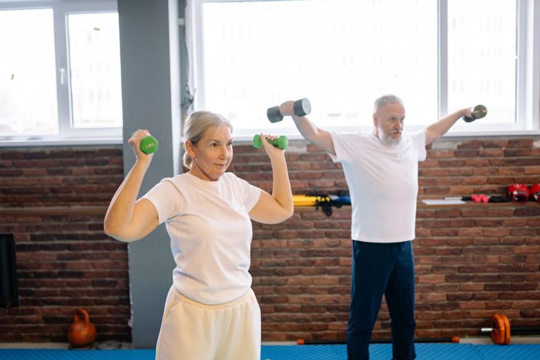 An older woman and man lifting light hand weights in a bright exercise studio