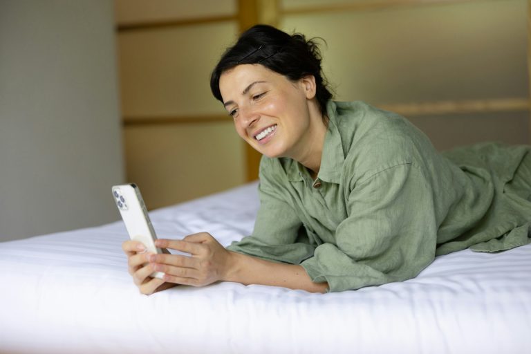 Woman lying on a bed in the morning looking at her phone